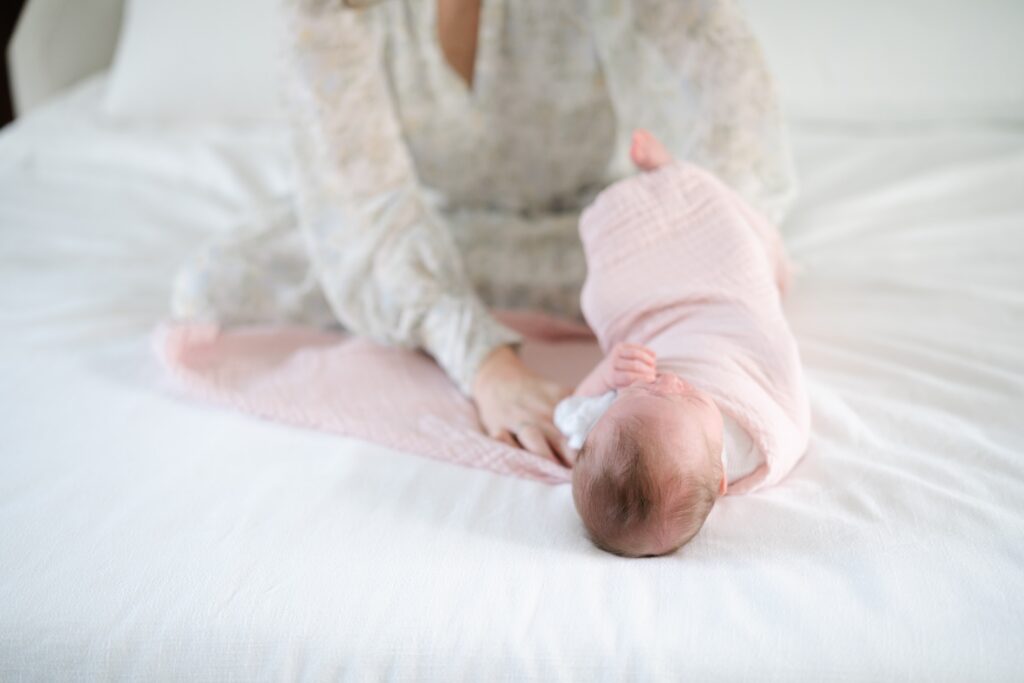 Newborn girl in a pink swaddle on a white bed during an in home newborn session in Nashville TN