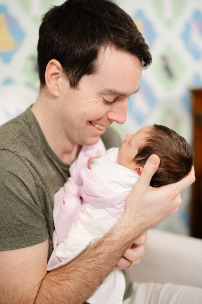 Father gazing at his newborn daughter during a relaxed in-home newborn photography session.