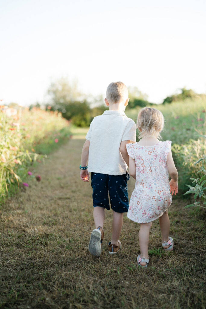 Brother and sister walking together between colorful flower rows during Nashville summer mini sessions