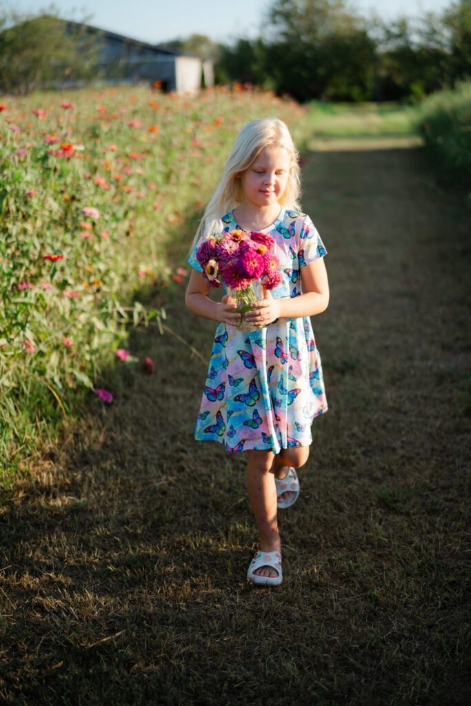 Young girl carrying a colorful bouquet while walking beside rows of summer flowers at Perry Family Farm