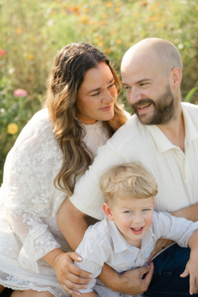 Family of three cuddling together among colorful flowers during Nashville summer mini sessions