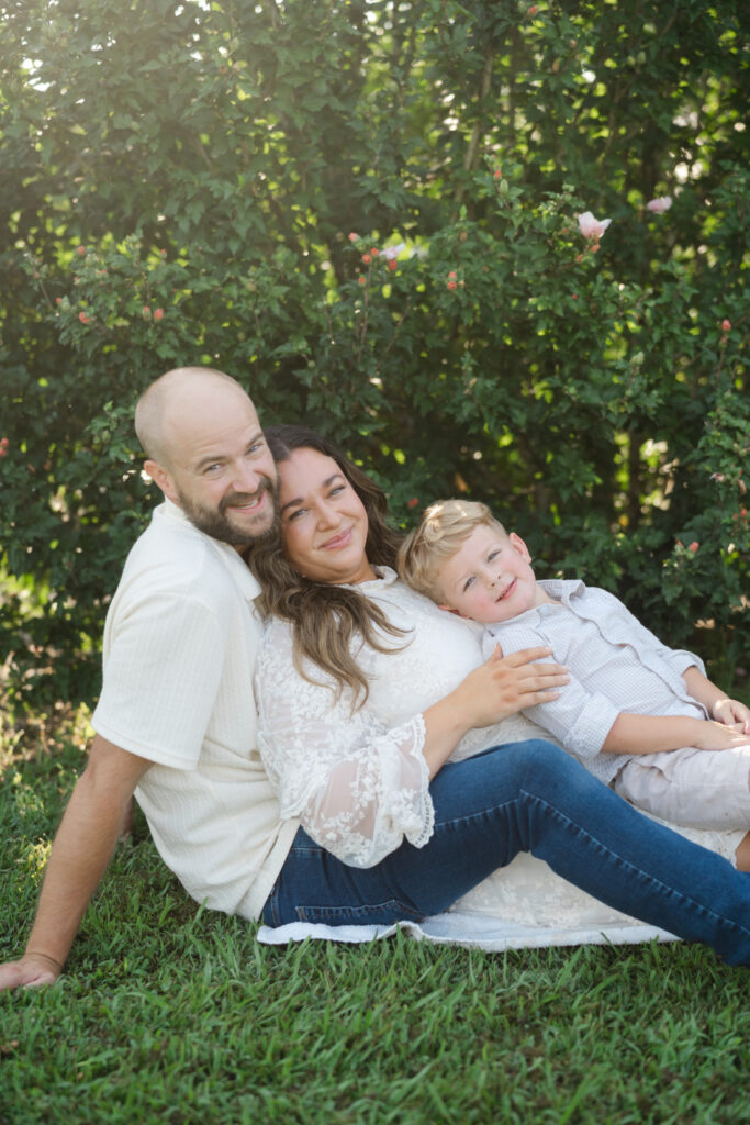 Mom, dad, and young son cuddling together on the grass during a relaxed summer family photo session